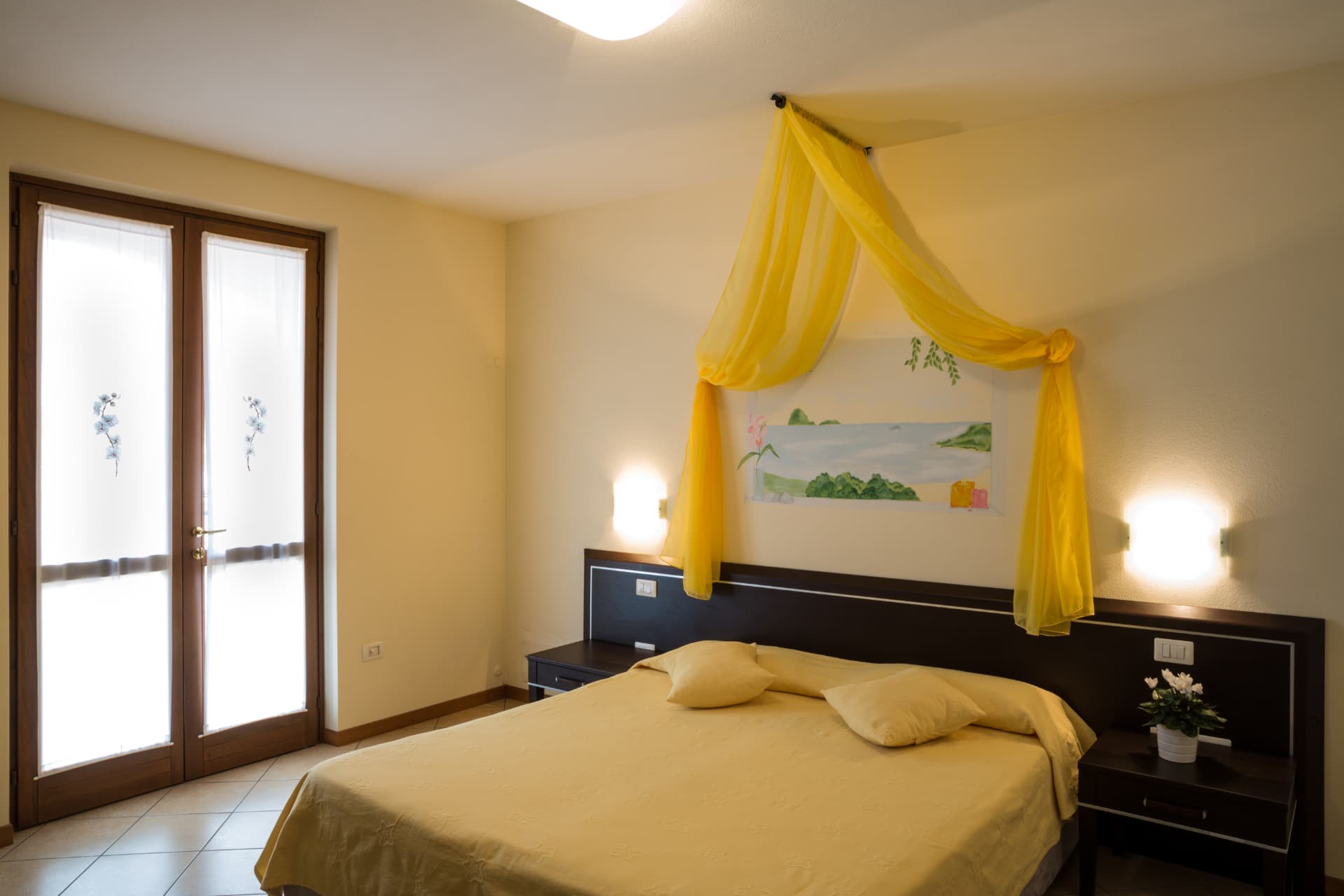 Camera delle orchidee: letto con copriletto giallo e baldacchino giallo sotto l'affresco di paesaggio marino