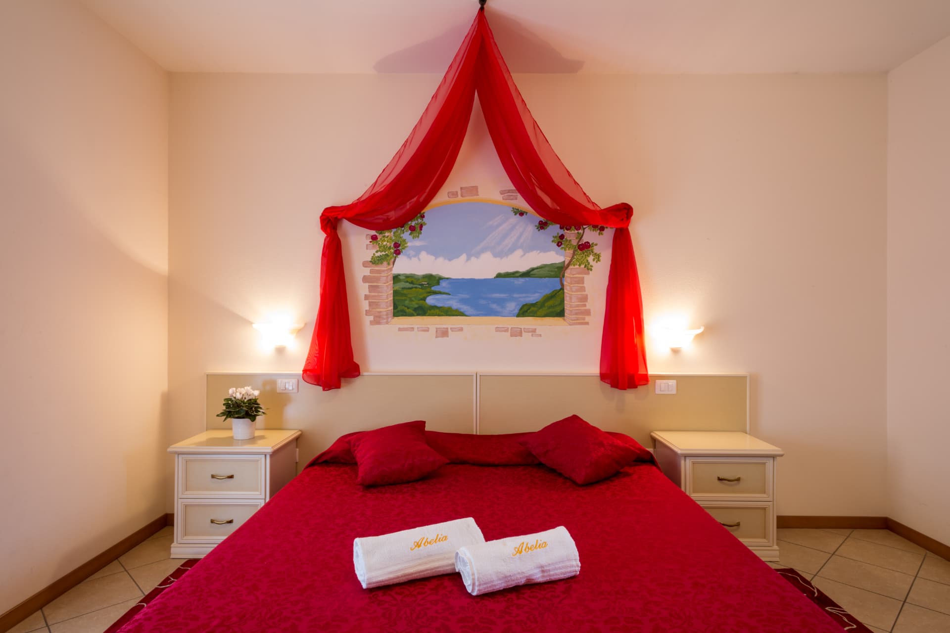 Camera delle Rose: letto con copriletto rosso e baldacchino sotto l'affresco del lago