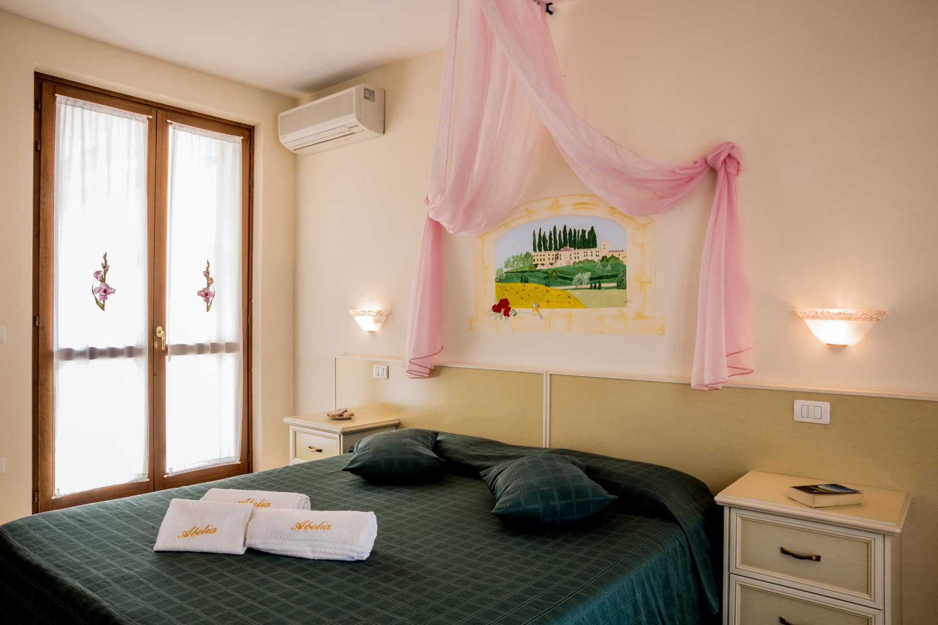 Camera dei gladioli: letto con copriletto verde scuro e baldacchino rosa sotto l'affresco di casale e cipressi