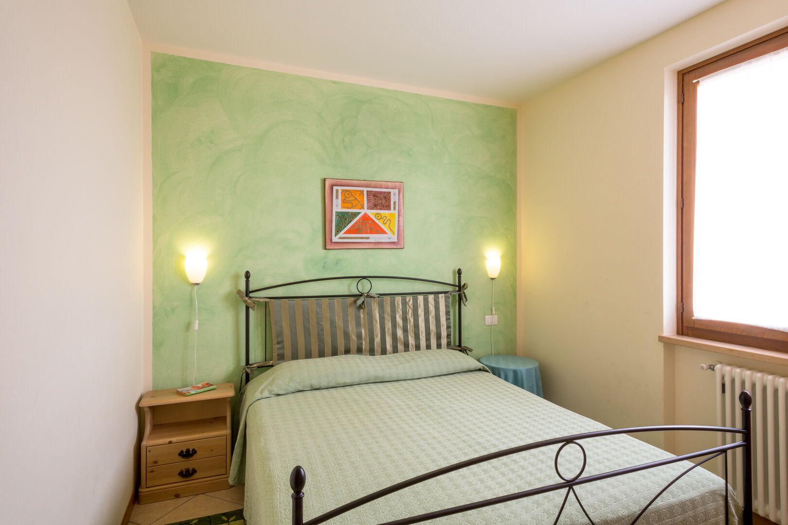 Appartamento Gli olivi: camera con letto in ferro battuto, copriletto verde e quadro a parete